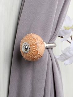 a close up of a curtain with a wooden knob on it's side and white flowers in the background