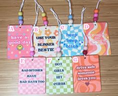 four tags with different sayings hanging from strings on a wooden floor, some have beads