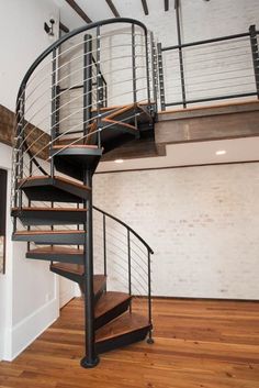 a spiral staircase in an empty room with wood floors and white brick wall behind it