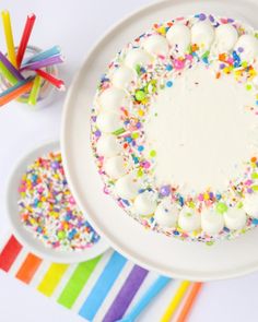 a cake with sprinkles and white frosting sitting on a plate next to colorful straws