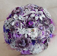 the bridal bouquet is adorned with purple and silver brooches, crystals and pearls