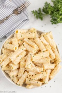 a white bowl filled with pasta and parsley on top of a marble countertop