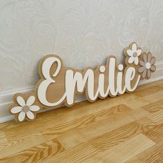 a wooden name sign with flowers on the bottom that says,'emlie '