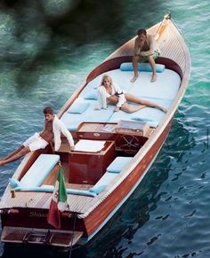 two people are sitting on the back of a boat in the water while another person is laying down