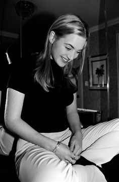 a black and white photo of a woman sitting on a bed with her hands in her pockets