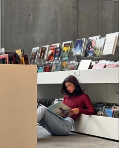 a woman sitting on the floor reading a book in front of a bookshelf