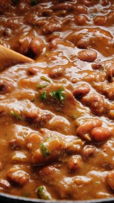 beans and meat are being cooked in a large pot with a wooden spoon on the side