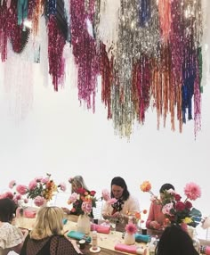 a group of people sitting around a table with flowers and cake on top of it