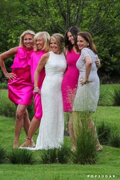 four women in pink dresses posing for a photo together on the grass with trees and bushes behind them