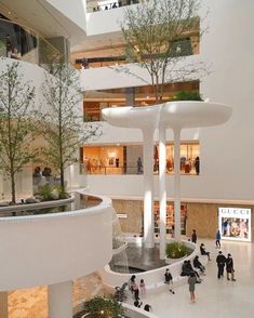 people are walking around in the atrium of a large building with trees and plants on it