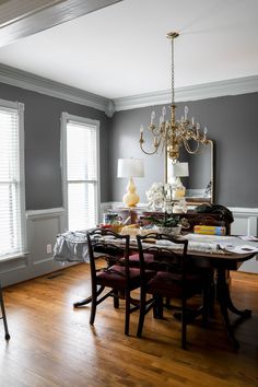 a dining room table with chairs and a chandelier hanging from the ceiling in front of two windows