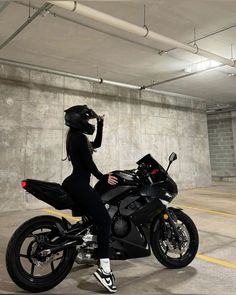 a woman sitting on top of a black motorcycle in a parking garage with her helmet on