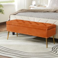 an orange bench sitting on top of a rug in front of a white and gray bed