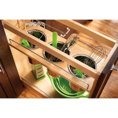 an open drawer with green dishes and utensils in it on a wooden floor