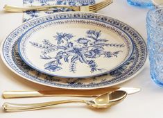 a blue and white plate with flowers on it next to gold utensils, glasses and silverware