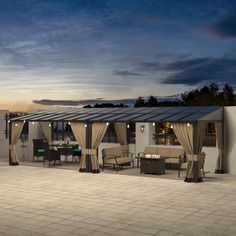 an outdoor dining area with patio furniture and curtains on the side of it at dusk