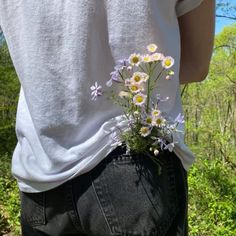 a person with their back to the camera, holding flowers in their jeans and wearing a white t - shirt