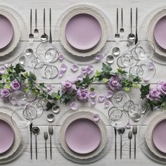 the table is set with pink plates, silverware and purple flowers on top of it