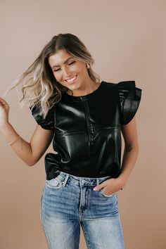 The Faux Leather Ruffle Sleeve Top in Black, is a bold and edgy piece to elevate your spring wardrobe. Perfect for transitioning from day to night, this top can be paired with high-waisted jeans and sneakers for a casual daytime look or dressed up with a skirt and heels for a night out on the town. Faux Leather Ruffle Sleeve Top Round neck Shirring detail Zipper at back Fabric Contents: 55% POLYESTER 45% POLYURETHANE Made in USA Model Specs: Emily is wearing a size small in the photo.How will this item fit you? Check out our MODEL SPECS (Typical Sizing - Karli: S-Size 5/26 - 5ft 2in, Emily: S-Size 3/25 - 5ft 5in, Syd: L/XL- Size 15/ - 5ft 8in)﻿Need help with sizing? No problem! Join our VIP group on Facebook, Everyday Chic Boutique VIP Insiders to chat directly with our team and other cust Leather Tops Outfit, Leather Top Outfit, Leather Tops, Ruffle Sleeve Top, Vip Group, Everyday Chic, Ruffled Sleeve Top, Top Round, Spring Wardrobe