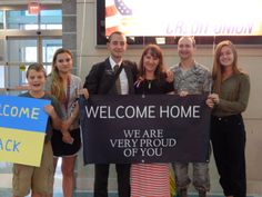 a group of people standing around each other holding up a welcome home sign in an airport