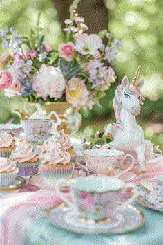 a table topped with cupcakes and unicorn figurines next to a vase filled with flowers