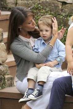 a woman holding a small child in her lap while sitting on a stone bench with other people