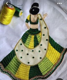 a woman in a green and yellow dress next to some spools of thread