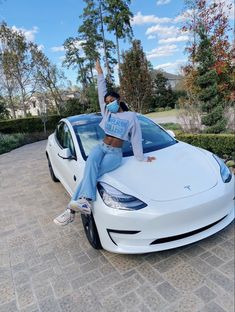 a woman sitting on the hood of a white car with her arms in the air