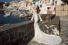 a woman in a white wedding dress standing on a stone wall next to the water