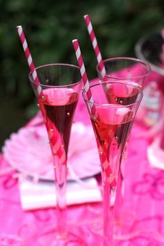 three glasses with pink liquid are sitting on a doily and one has two straws in it