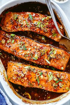 baked salmon with sesame seeds and seasoning in a white casserole dish on top of a blue towel