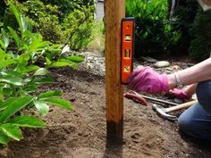 a woman kneeling down next to a wooden pole with gardening tools on top of it