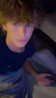 a young man sitting on top of a bed next to a pillow