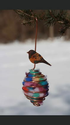 a bird is perched on top of a colorful ornament hanging from a tree