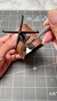 two hands are working on a piece of wood that has been carved into the shape of a cross