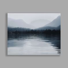 a large body of water with mountains in the background and foggy skies above it