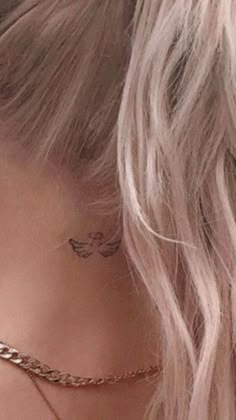 the back of a woman's neck with a small angel tattoo on her left side