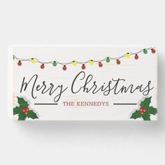 a wooden sign with christmas lights and holly berries on it that says merry christmas the kennedys