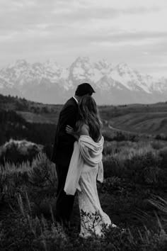 a bride and groom embrace in front of the snow - capped mountains on their wedding day