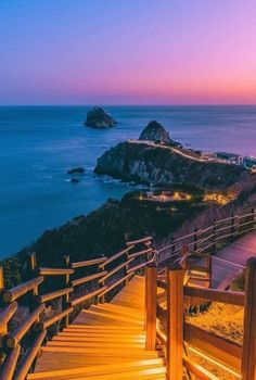 a wooden walkway leading to the ocean at dusk with lights shining on the railings