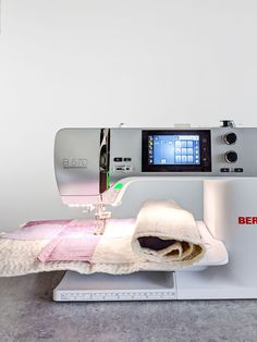 a sewing machine with a piece of cloth on it's side and a digital screen in the background