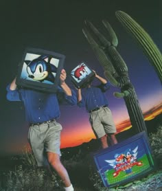 two people holding up video games in front of a cactus plant and television screen with sonic the hedgehog on it