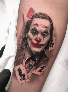 the joker tattoo on the leg is very realistic and colorful, it looks like he's holding playing cards