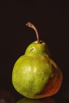 two pears sitting next to each other on top of a black surface with a dark background