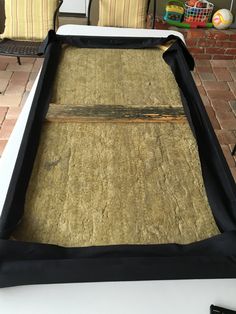 a bed frame is covered with straw and black fabric for protection from the sun on a brick patio