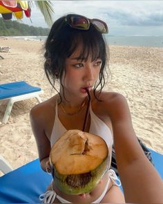 a woman sitting on the beach eating a large sandwich with a straw in her mouth