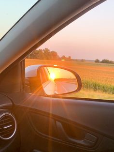 the sun is setting in the side mirror of a car as it drives past an open field