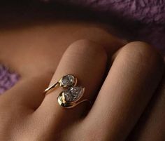 a woman's hand wearing a gold ring with two diamond hearts on the side