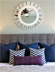 a bed with blue and white pillows in front of a round mirror on the wall