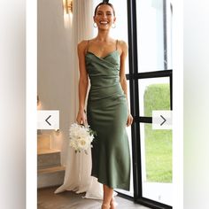 a woman standing in front of a window wearing a green dress and holding a bouquet